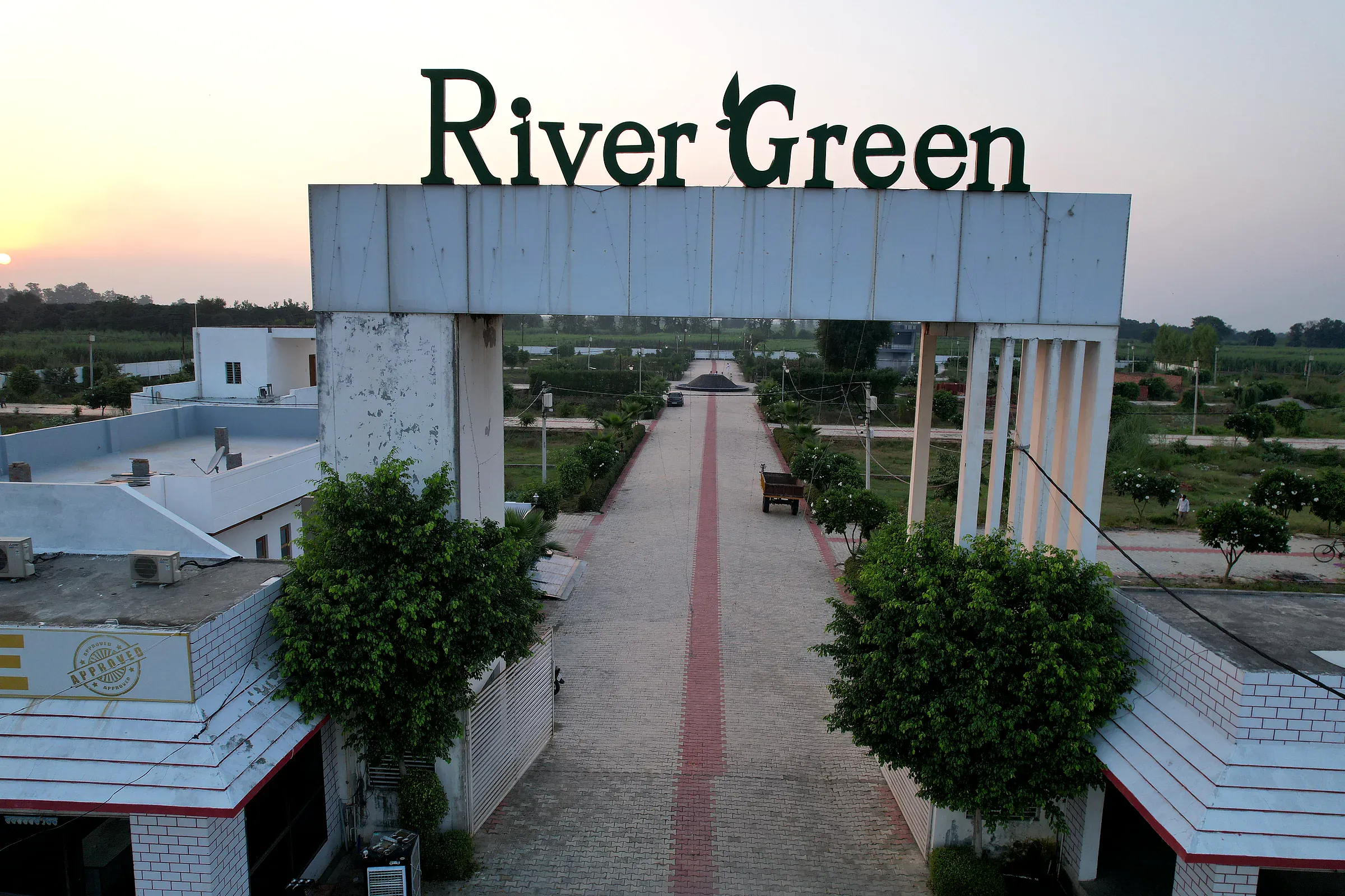 River Green lettering on the entrance arch at sunset, with the boulevard running into the colony