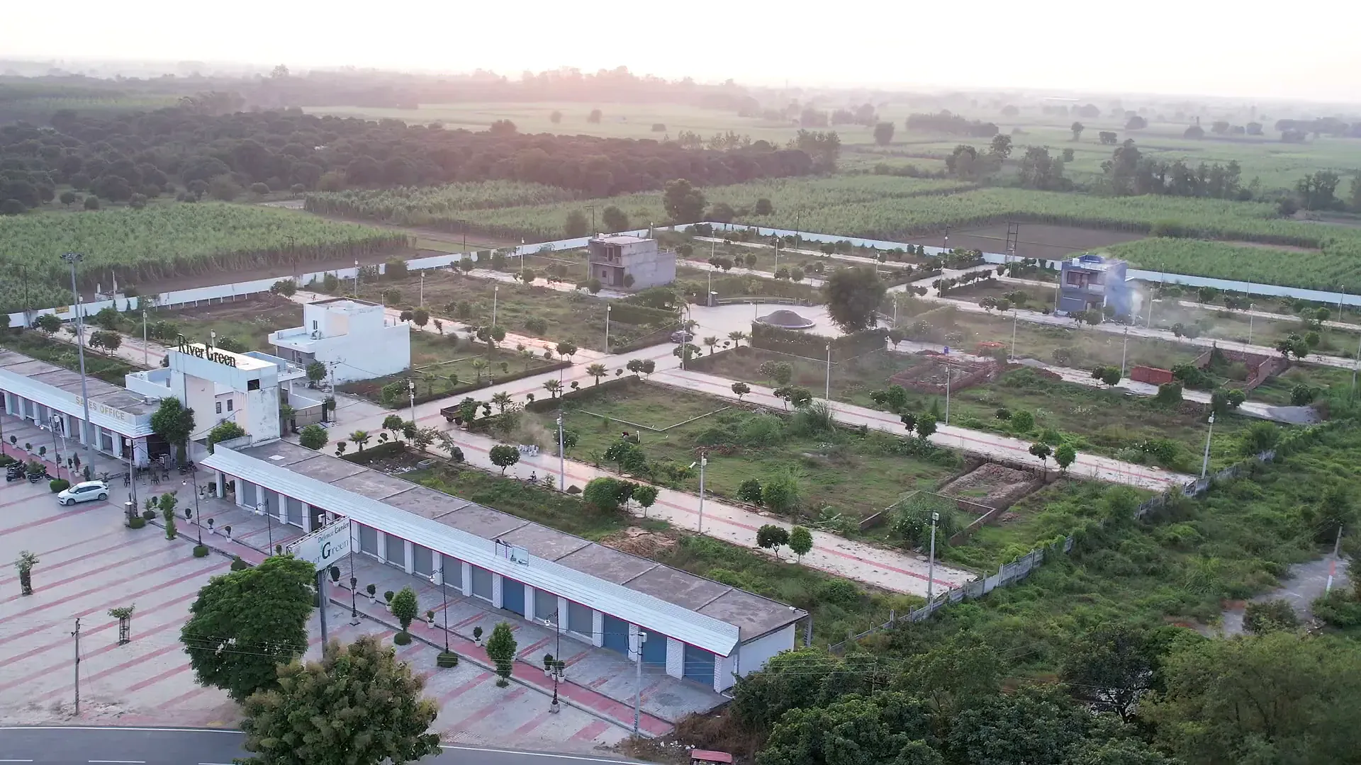 Evening aerial over River Green Society: the shopping arcade, tree-lined streets and plots stretching to the fields