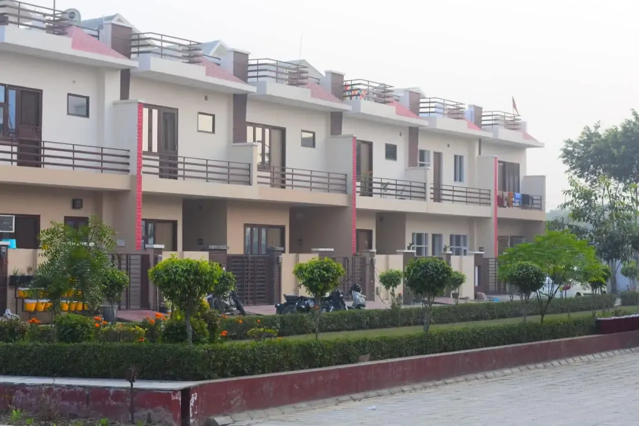 Ganpati Enclave: row of cream villas with red-tiled roofs behind a landscaped hedge strip