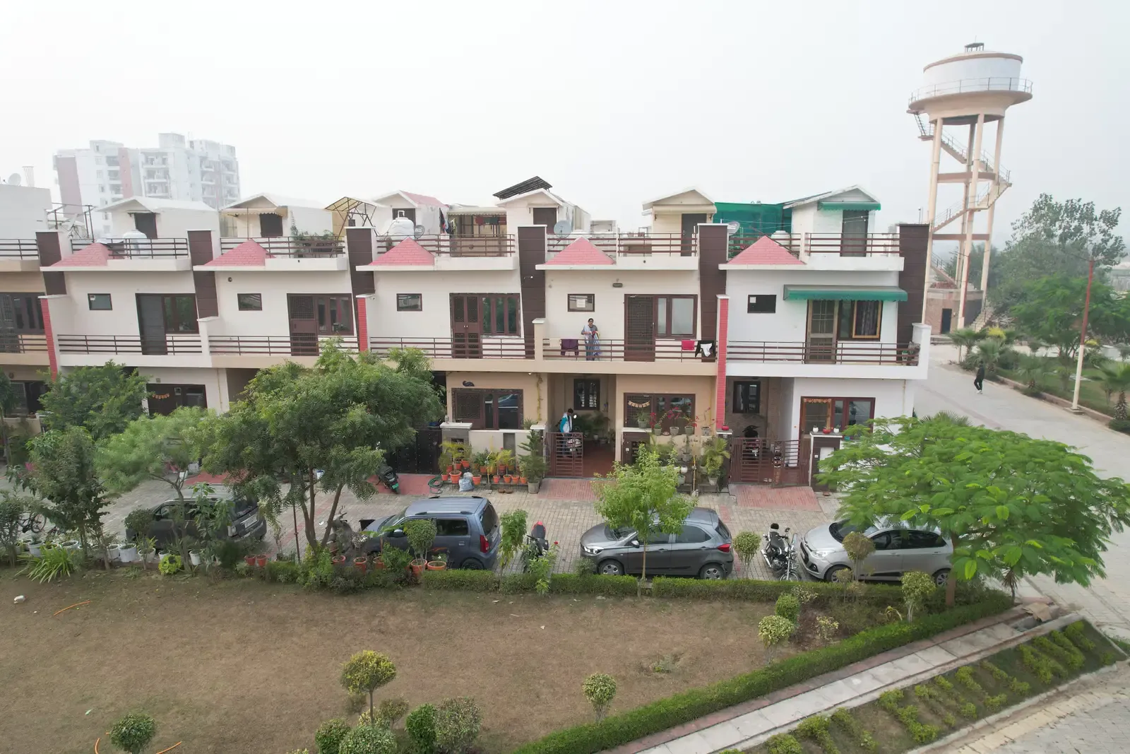 Ganpati Enclave: elevated view of a terrace of townhouses facing a landscaped park, a water tower beyond