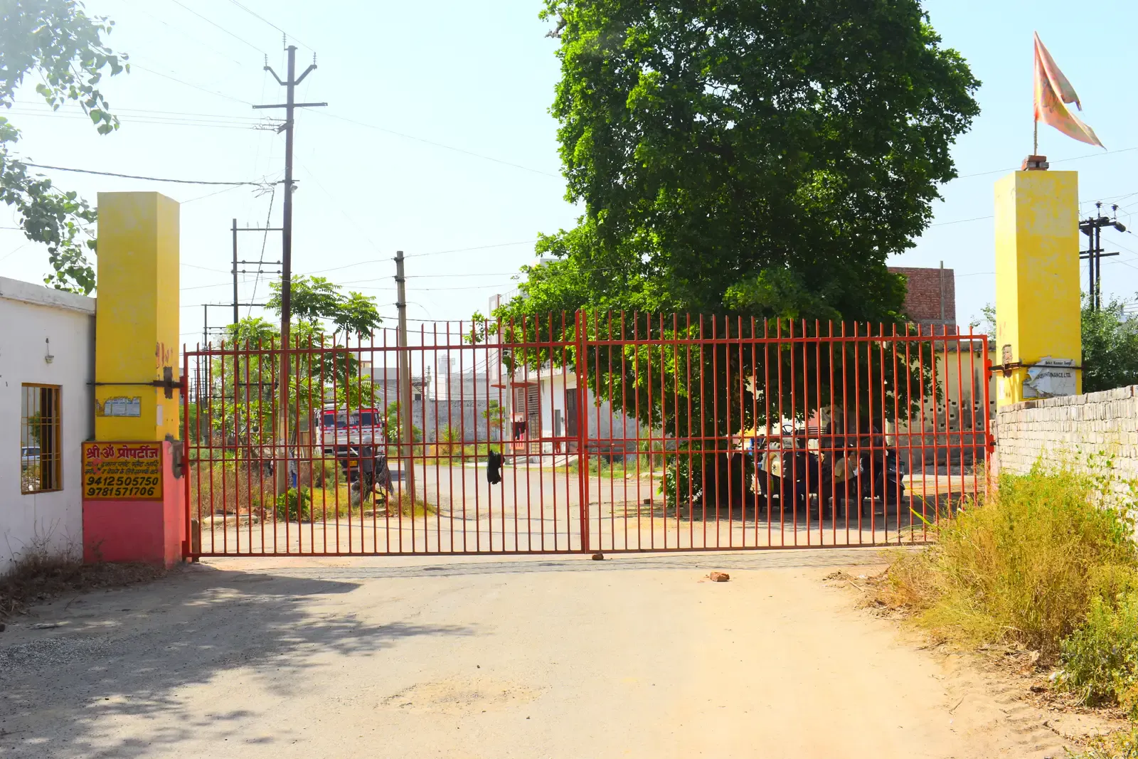 Defence Kunj entrance with red metal gates between yellow pillars