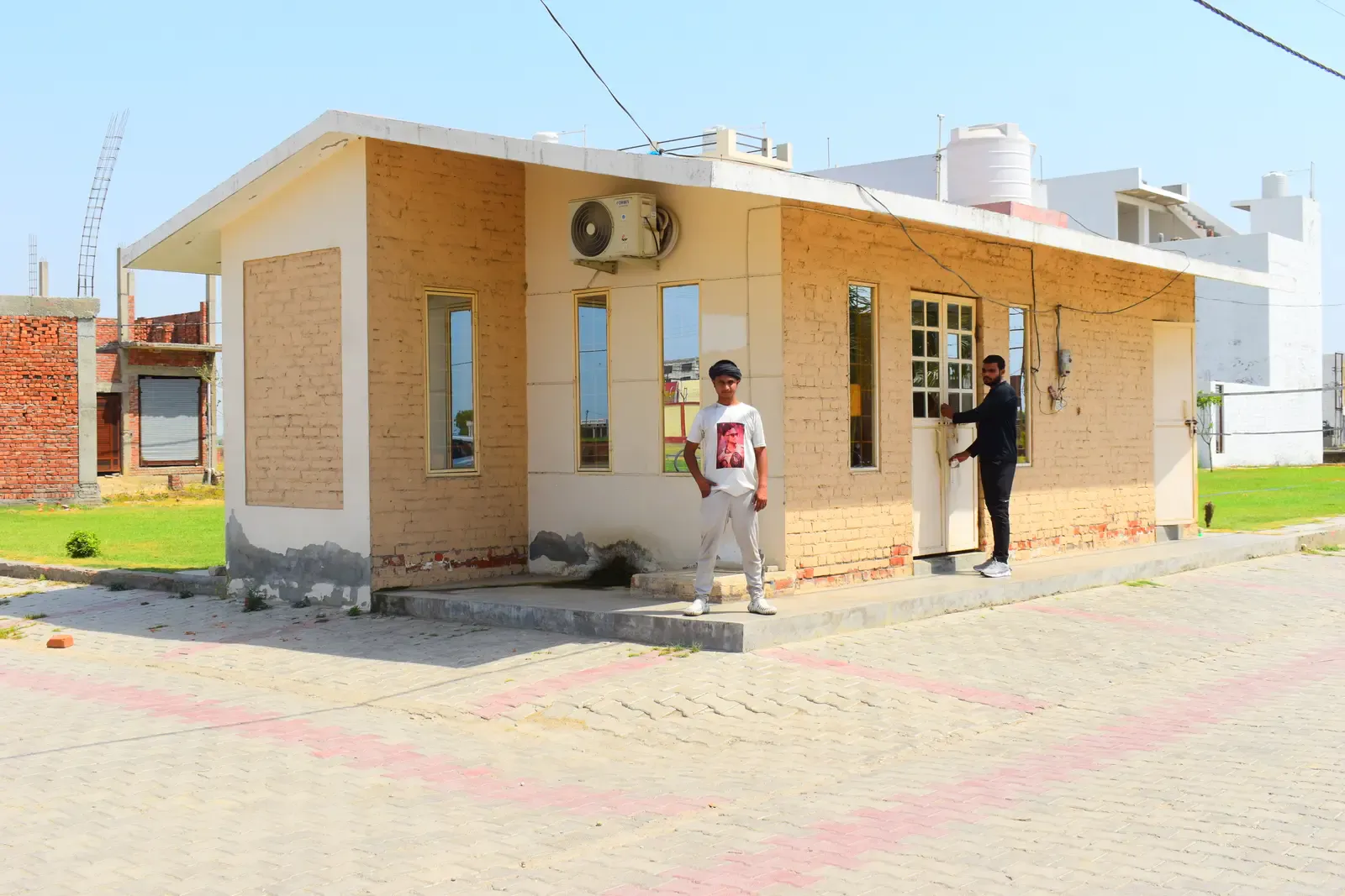 Basant Kunj: small brick-clad site office with two men standing outside