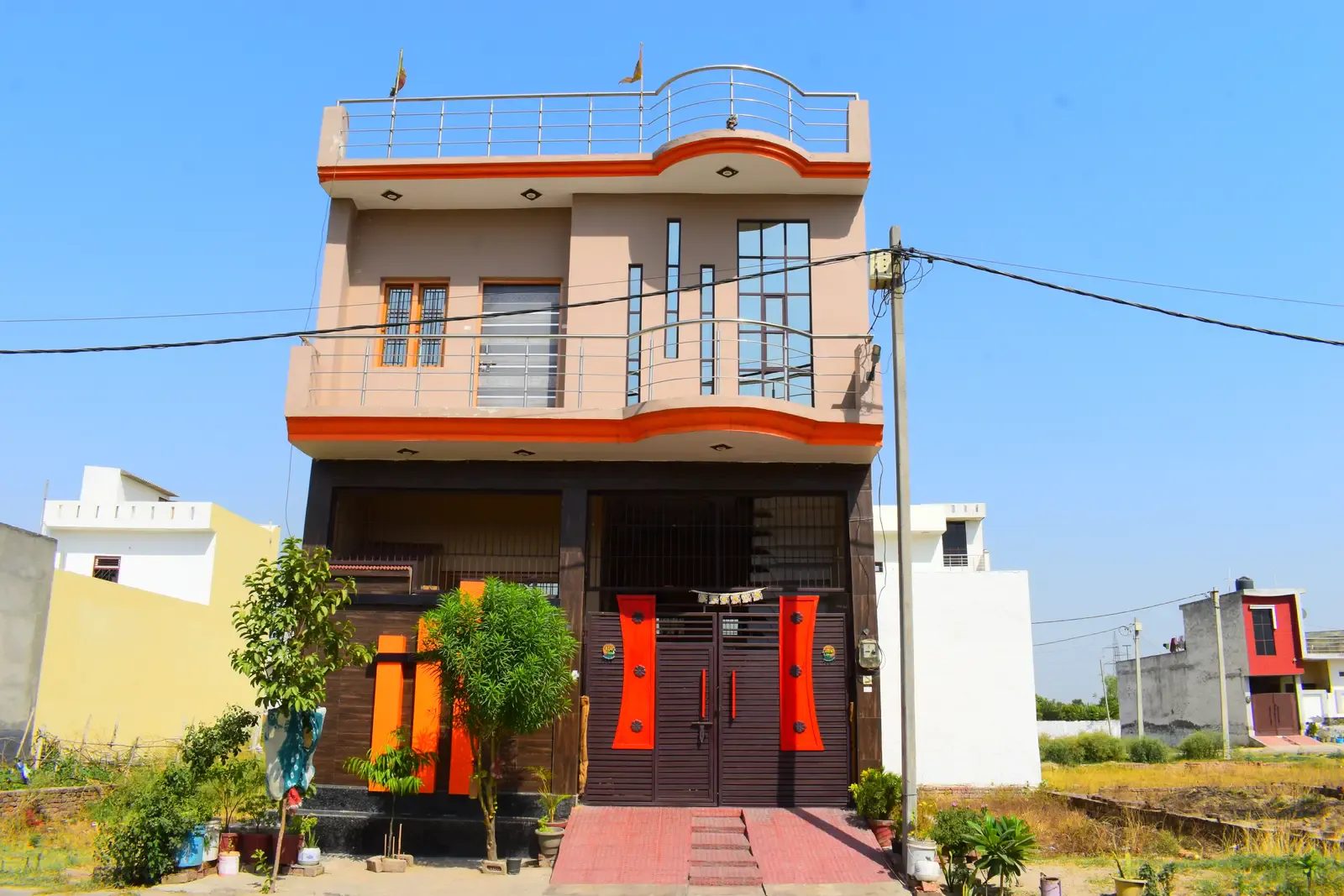 Defence Kunj: two-storey home with a beige-and-orange facade and red doors