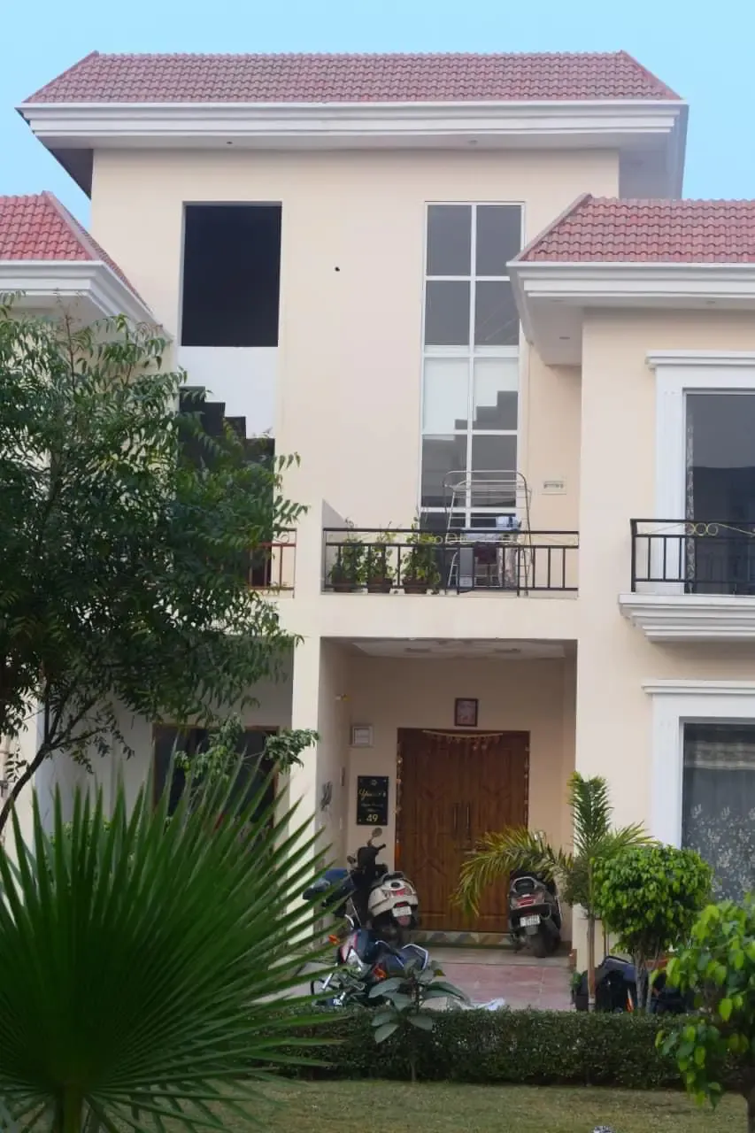 Ganpati Enclave: cream two-storey villa with a red-tiled roof and a fan palm in front