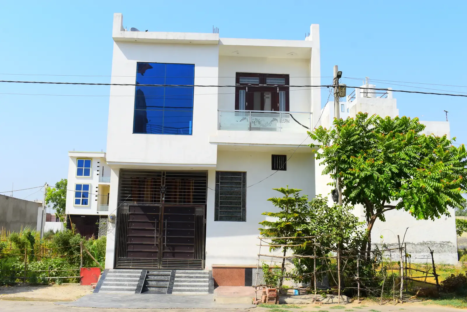 Defence Kunj: white two-storey home with a blue glass window and garden trees