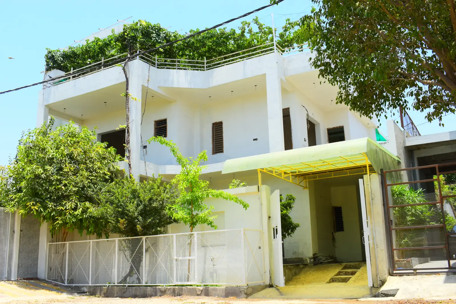Defence Garden Meerut: two-storey white home with a green awning, garden trees and a white fence