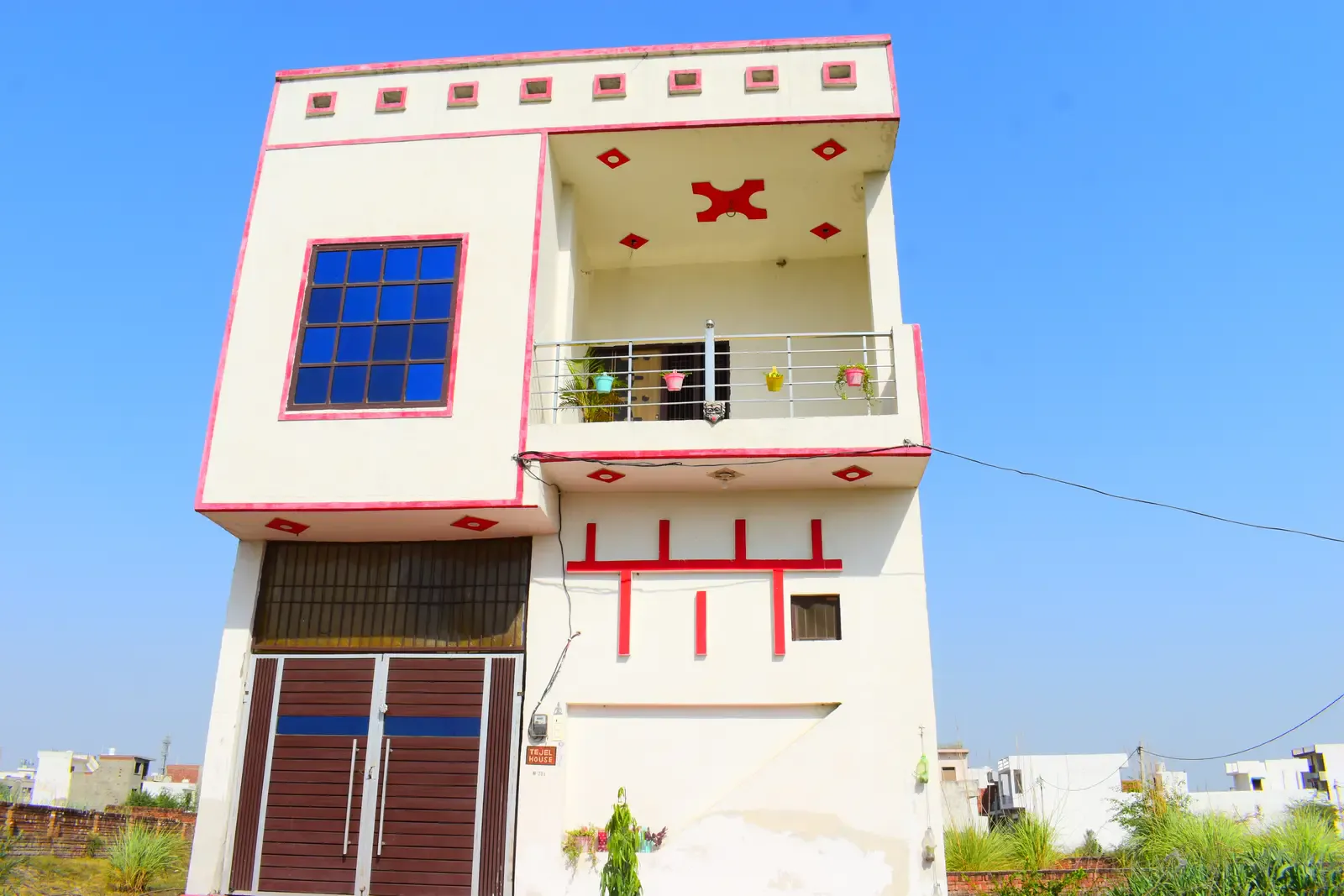 Defence Kunj: narrow cream house with red decorative motifs and a balcony of potted plants