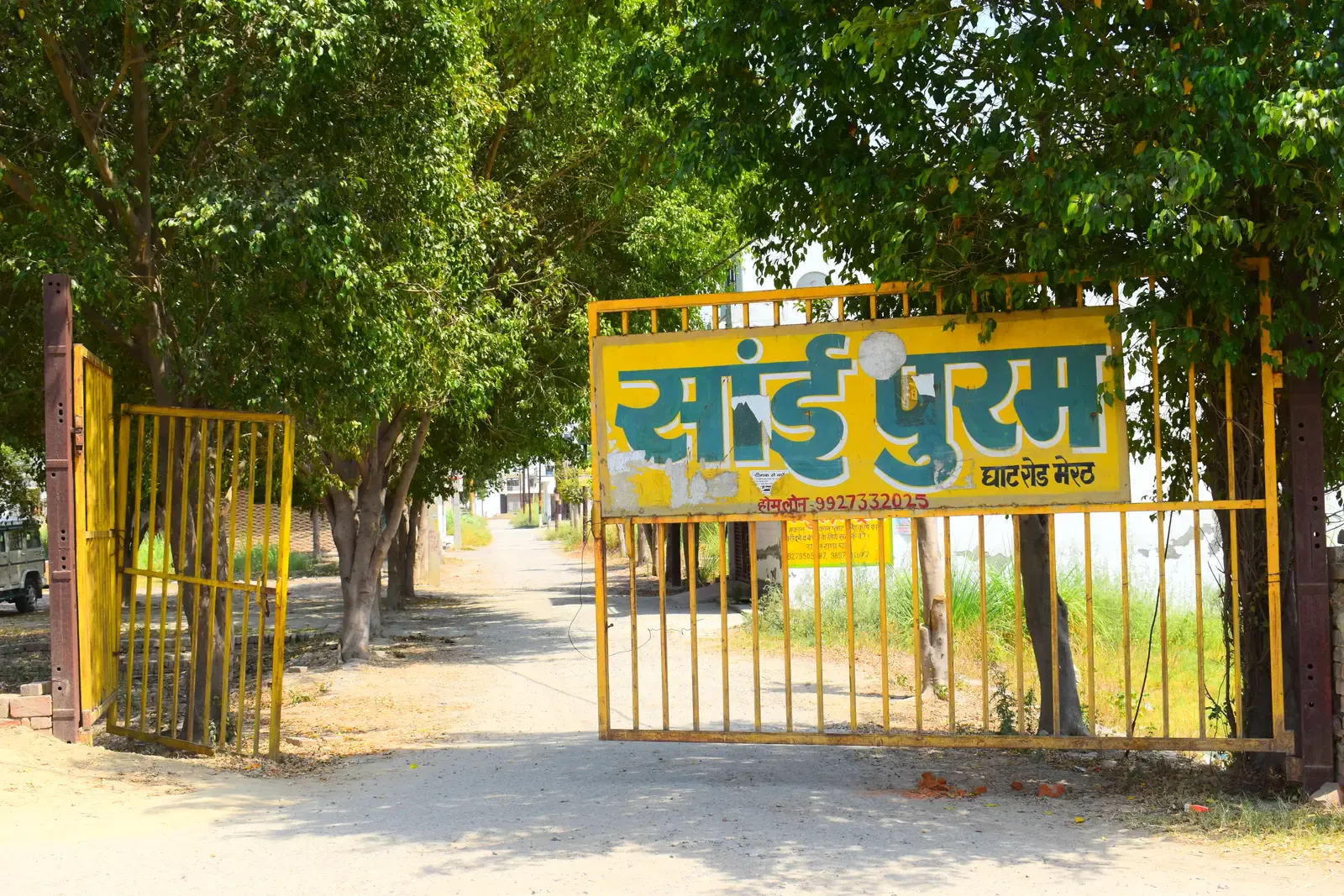 Saipuram entrance gate with the yellow Saipuram signboard and a tree-lined road