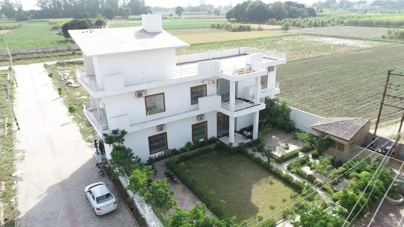 Aerial view of a large white three-storey house with a walled lawn garden beside open fields