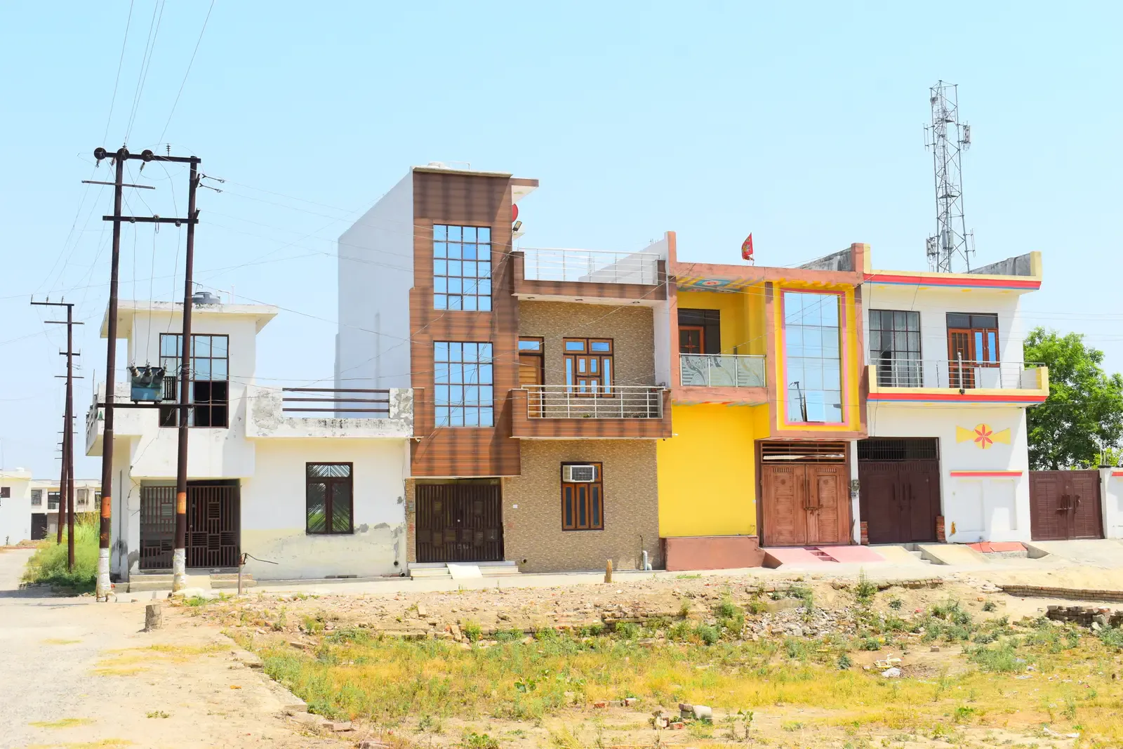 Saipuram: row of colourful homes with wood-panel and yellow facades across an open plot