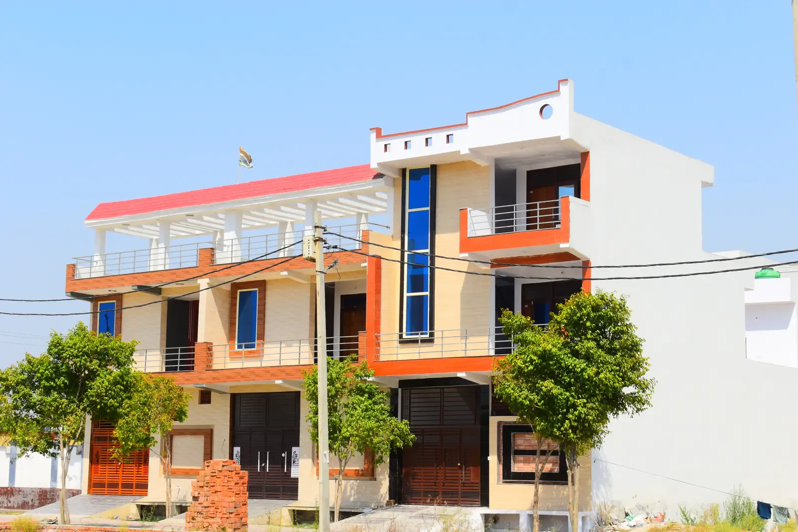 Basant Kunj: two-storey homes with orange trim and blue glass details under a clear sky