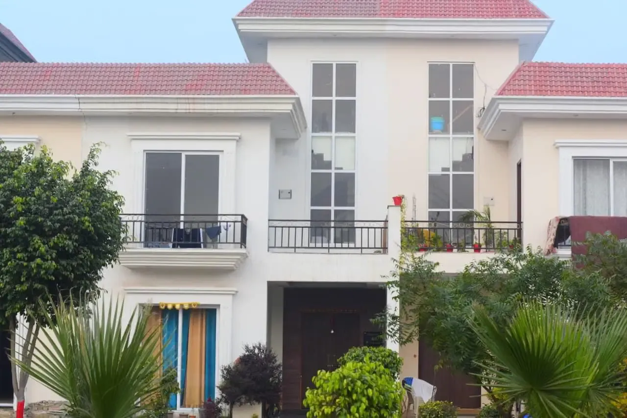 Ganpati Enclave: cream villa with tall windows behind fan palms and shrubs