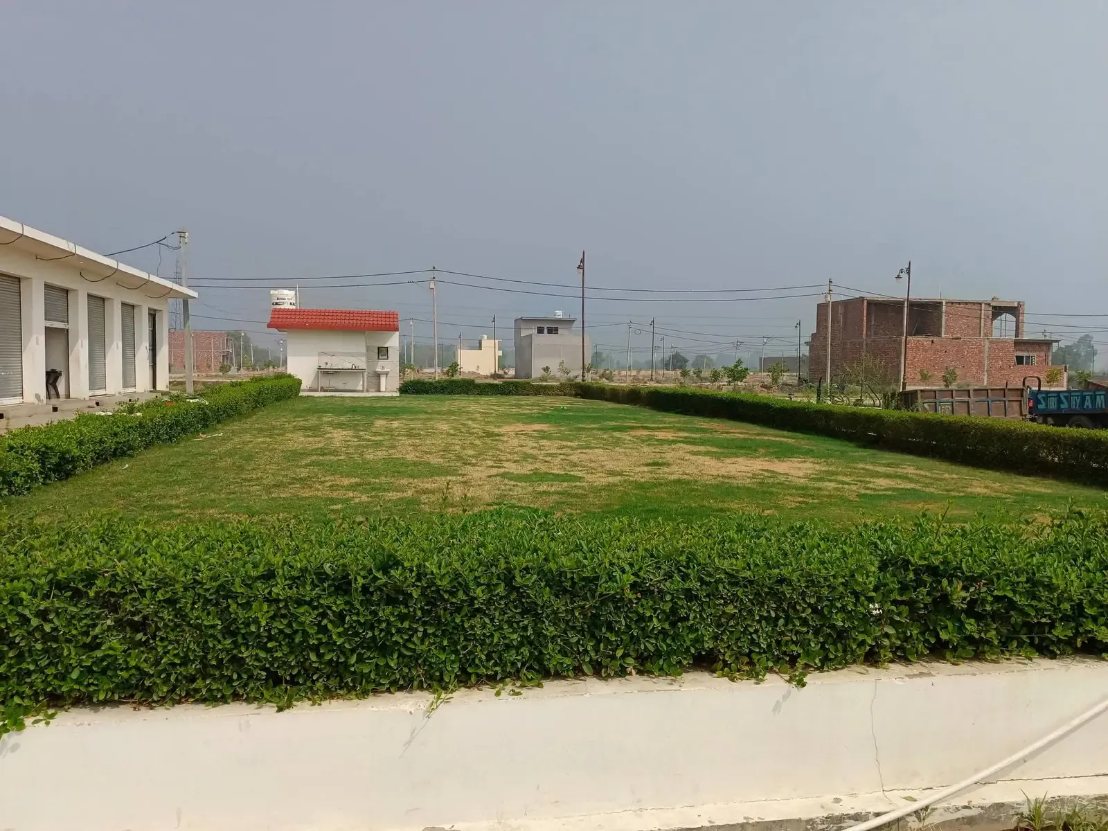 Defence Garden Phase 2: hedged park lawn with shops and a guard post beyond