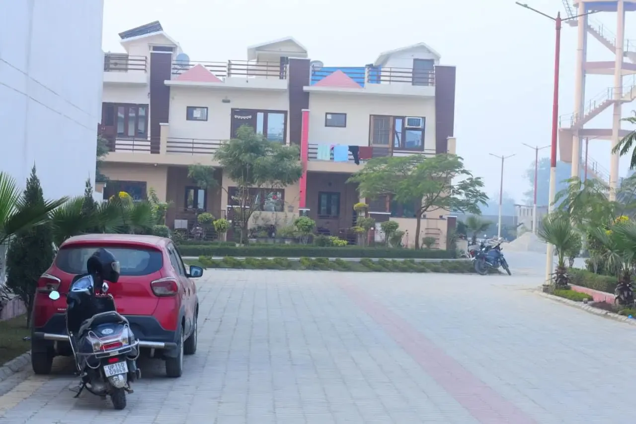 Ganpati Enclave: paved courtyard road with a parked car and scooter in front of townhouses