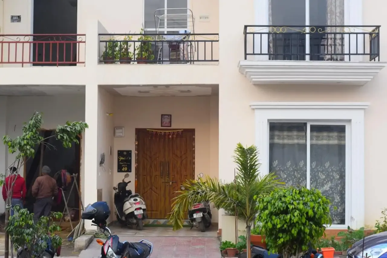 Ganpati Enclave: villa entrance with a carved timber door, residents and parked scooters